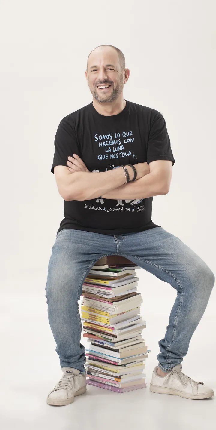 Alejandro Schujman sentado sobre una pila de libros, riendo