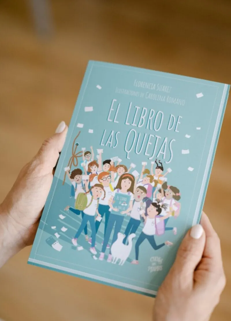 Manos sosteniendo El libro de las quejas, de Florencia Suarez, con ilustraciones de Carolina Romano